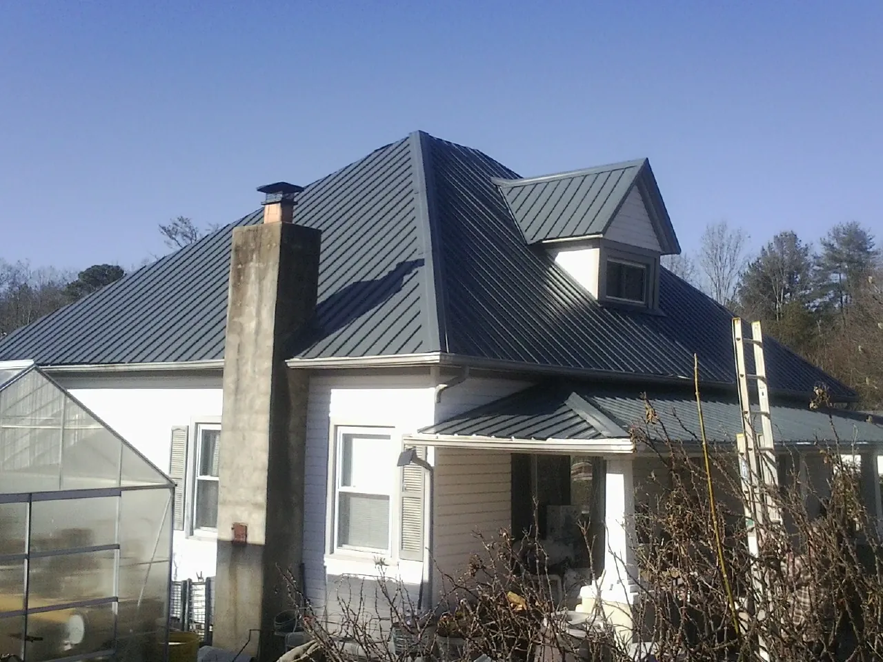 Dark blue standing seam metal roof on a white farmhouse with dormer — Slate & Tile Roof Repair by Roofing Brothers in Wright City