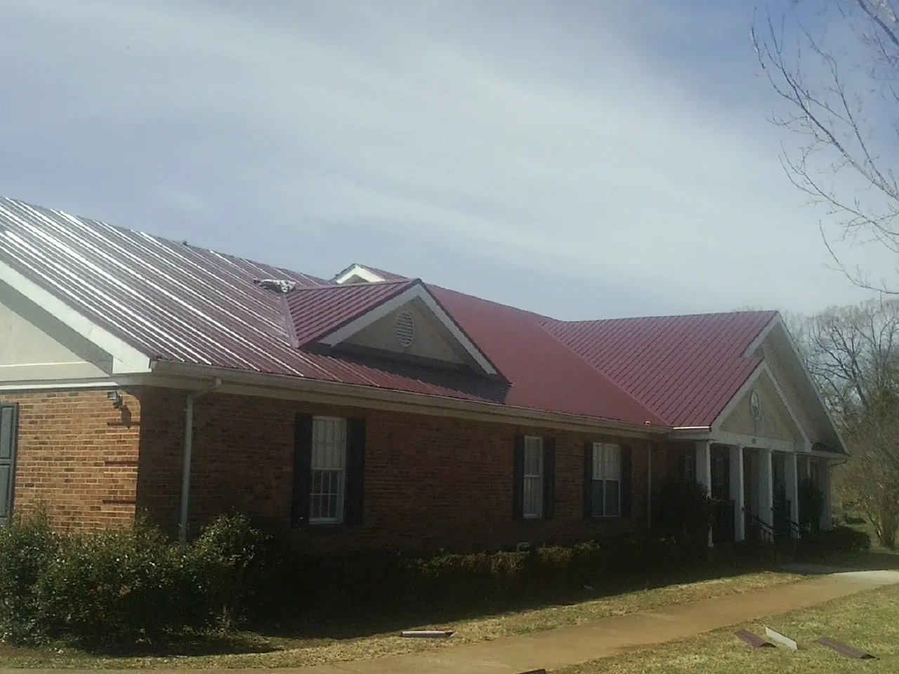 Red metal roof with gabled entries on a long brick building, from a Hail Damage Roof Repair job in Wright City