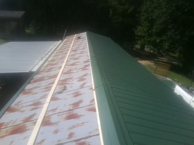 Old rusted panels beside newly installed green metal roofing — Wind Damage Roof Repair by Roofing Brothers in Wright City