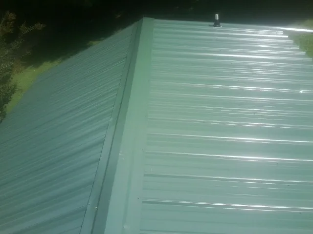 New green metal panels meeting at the ridge of a roof — Flat Roof Repair work by our crew in Wright City