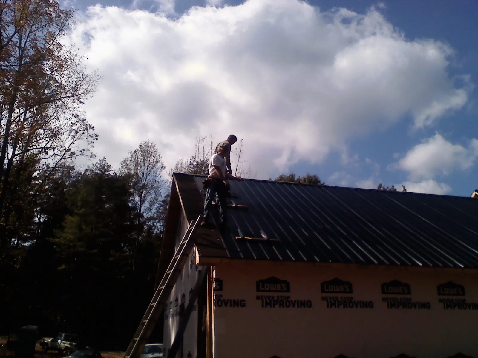 Roofer fastening dark metal panels high against a cloudy sky, from a Roof Inspection job in Wright City