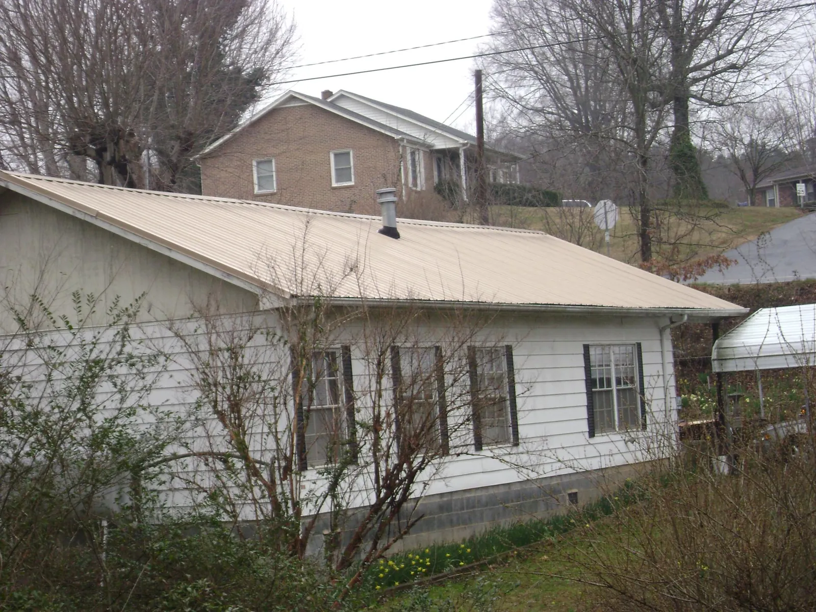 Tan metal roof on a white sided house set into a hillside — Commercial Roofing by Roofing Brothers in Wright City