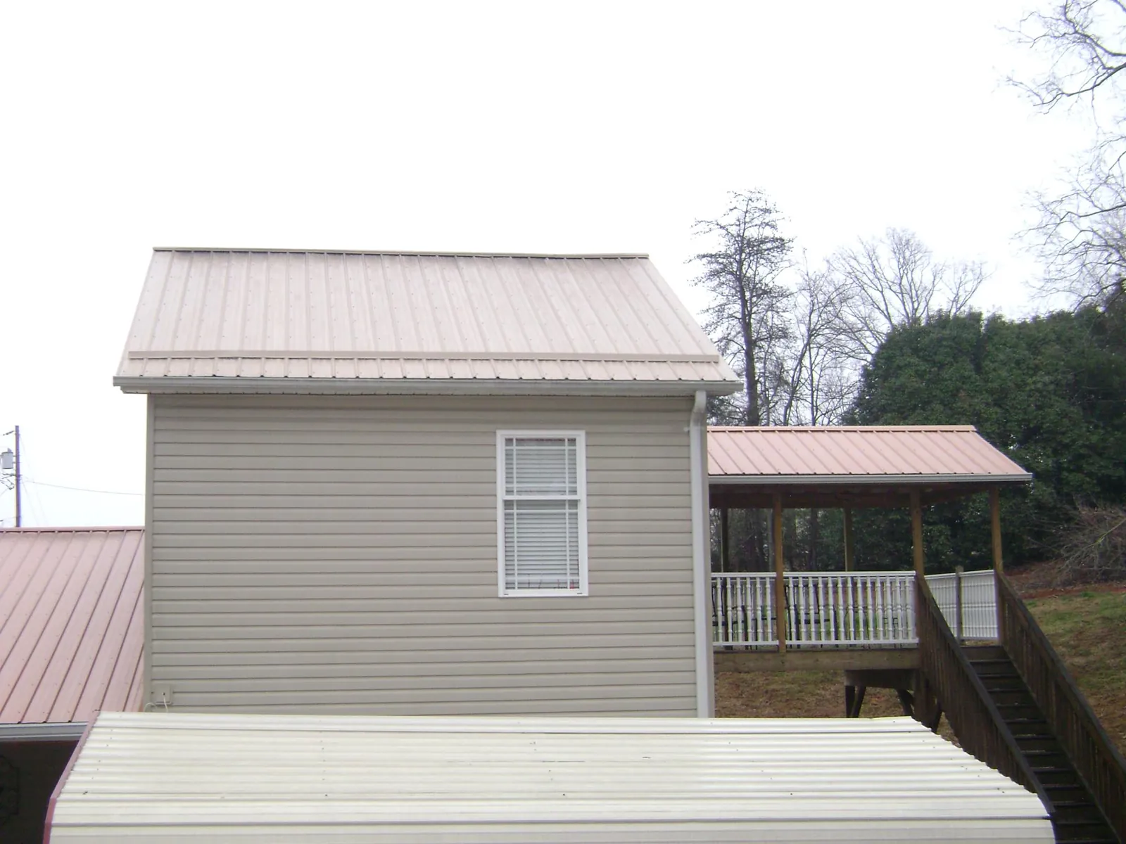 Tan metal roofs on a two story addition and attached porch, from a Roof Replacement job in Wright City